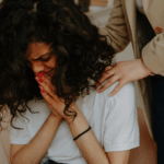 A woman sits on a couch, tears streaming down her face as she cries.