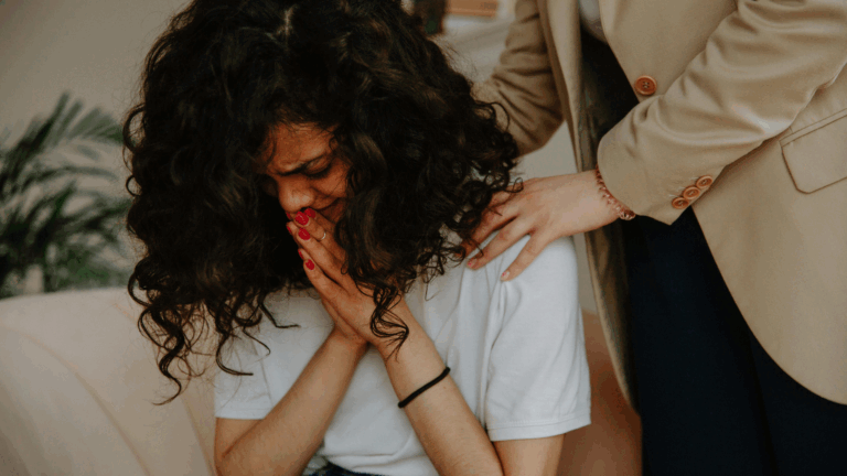 A woman sits on a couch, tears streaming down her face as she cries.